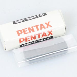 以下が含まれることがあります： 白い箱に「PENTAX REMOTE CONTROL D SET」と印刷されています。箱には黒いリモコンが入っています。