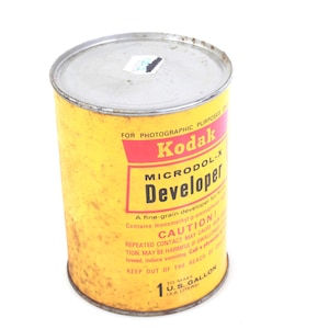 Pode incluir: Uma lata de revelador Kodak Microdol-X vintage. A lata cilíndrica é amarela com um rótulo vermelho e branco. O rótulo diz "Kodak Microdol-X Developer" e inclui um aviso. A lata foi projetada para fazer 3,79 litros.