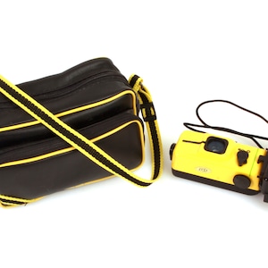 以下が含まれることがあります： 黄色と黒色の水中カメラと、それに合わせた黒色のバッグ。 カメラには黒色のフラッシュがあり、バッグには黄色のストラップとトリムが付いています。 カメラには「Wet-f ADI」と表示されています。