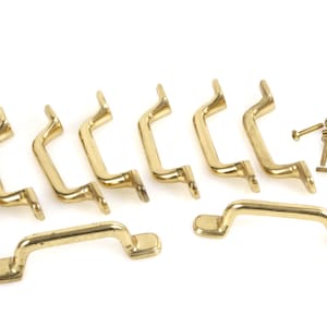 May include: A set of eight brass-coloured cabinet pulls and a pile of matching screws. The pulls have a curved handle design with rectangular mounting plates. The hardware is likely for furniture restoration or new construction.