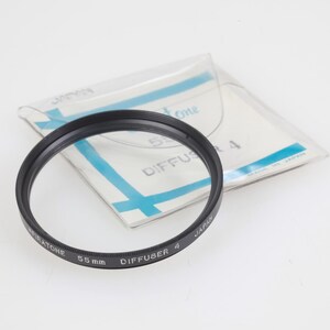 May include: A black 55mm camera lens filter with the text "MIRATONE DIFFUSER 4" and "JAPAN" printed on the rim. The filter is in a clear plastic sleeve with blue accents and the text "DIFFUSER 4".