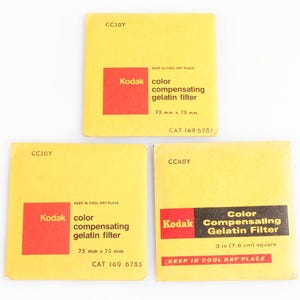 Op de afbeelding: Drie vintage Kodak kleurcompensatie gelatinefilters. Elke filter is vierkant, met een gele achtergrond en een rood Kodak-logo. De tekst bevat filtertype, afmeting (75 mm x 75 mm of 7,6 cm vierkant) en een catalogusnummer.