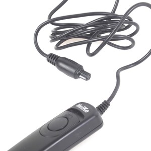 May include: A black Meike camera remote control with a coiled black cable and a connector. The remote has a button and the brand name printed on it. The background is white.