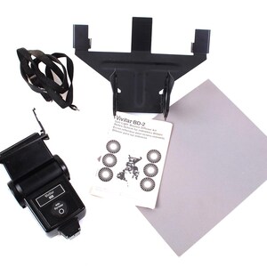 May include: A black Vivitar BD-2 flash light diffuser kit with a flash, mounting bracket, strap, reflector, and instruction manual. The instruction manual has the text "Vivitar BD-2" printed on it.