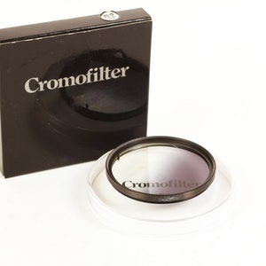 Puede incluir: Un filtro de cámara redondo, negro y plateado con la palabra "Cromofilter" impresa en él. El filtro está en una caja negra con el mismo texto impreso en ella.