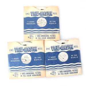 May include: Three vintage View-Master reel packets. Each packet is cream-colored with blue wave designs and text that reads "ONE VIEW-MASTER REEL" and "7 MORE WONDERS OF THE WORLD". The packets contain 7 three-dimensional pictures in full-color Kodachrome.