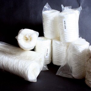 May include: A collection of white cylindrical water filter cartridges, some individually wrapped in clear plastic film. Several of the upright cartridges feature a white label with the black printed text PCP-10-4, indicating the specific model type.