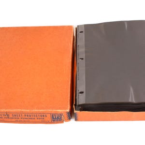 Può includere: Una scatola arancione aperta con proteggi fogli in acetato nero. La scatola ha il testo "Acetate Sheet-Protectors Reinforced-Punched Edge". I proteggi fogli sono perforati a tre fori.