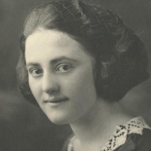 May include: A monochrome portrait of a woman with dark hair styled in a short bob. She wears a dark dress with a lace collar. The photograph is a close-up, focusing on her face and upper body, typical of vintage photography.