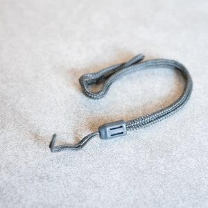 Puede incluir: Un cordón gris con un gancho de plástico y un cierre de plástico negro.