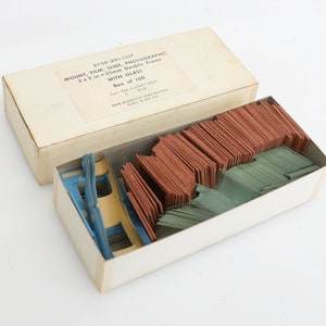 May include: A box of 100 2x2 inch, 35mm double frame photographic slide mounts with glass. The box is white with black text that reads "6750-291-5517 MOUNT, FILM, SLIDE, PHOTOGRAPHIC 2x2 in.-35mm Double Frame WITH GLASS Box of 100 ERIE SCIENTIFIC CORPORATION".