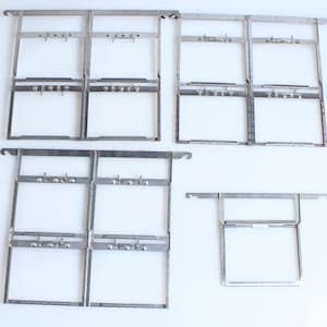 May include: A collection of silver metal frames, each with rectangular spaces and small hooks. The frames are laid out on a white background. They seem designed to hold items, perhaps pictures or art. The style is simple and industrial.