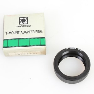 May include: A black T-mount adapter ring for Konica cameras, in its original box. The box is white with green accents and the text "Photoco T-Mount Adapter Ring" printed on it.