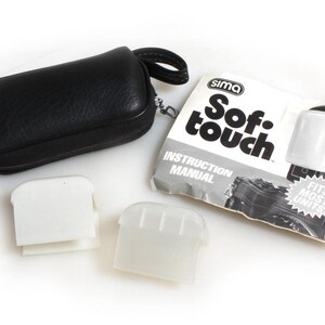 May include: A black leather case with a zipper, two white plastic camera lens filters, and a white instruction manual for a Sima Sof-touch camera lens filter. The manual has the text "Sima Sof-touch Instruction Manual Fits Most Units".