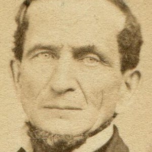 May include: A sepia-toned portrait of a man with a neatly trimmed beard and dark hair. He is wearing a dark jacket over a white collared shirt. The photograph is a vintage image, likely from the 19th century.