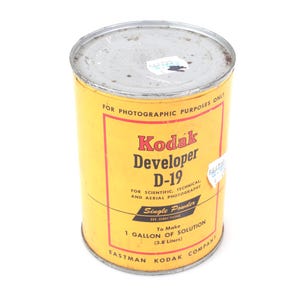 Op de afbeelding: Een vintage Kodak Developer D-19 blik met een geel en rood etiket. Het etiket bevat de tekst "FOR PHOTOGRAPHIC PURPOSES ONLY" en "1 GALLON OF SOLUTION (3,8 liter)". Het blik is cilindrisch met een zilveren deksel.