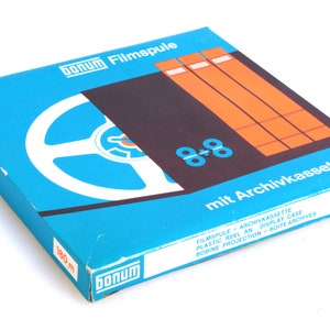 Può includere: Una scatola blu e arancione per un rotolo di pellicola da 8 mm. La scatola riporta la scritta "bonum Filmspule 8-8 mit Archivkassette" e "180 m 600 ft".