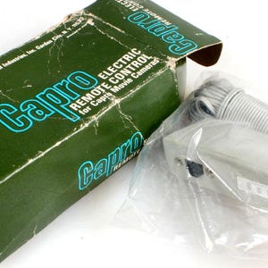May include: A green box with the text "Capro Electric Remote Control for Capro Movie Cameras" on it. The box contains a white remote control with a cord.