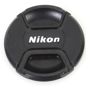 May include: Black camera lens cap with the word "Nikon" in white lettering.
