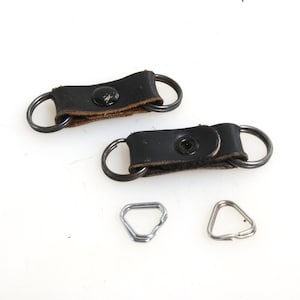 May include: Two black leather camera strap connectors with metal rings. Two silver metal D-rings are also included.