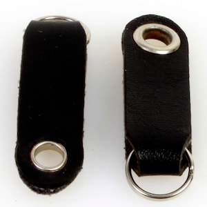 以下が含まれることがあります： 銀色の金属製のリングとハトメが付いた黒い革製のキーホルダーが2つ