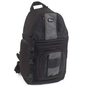 Puede incluir: Mochila negra para cámara con detalles en gris. Cuenta con un asa superior, múltiples compartimentos y correas ajustables. La bolsa tiene un bolsillo frontal rectangular y una parte trasera acolchada. El logotipo de Lowepro es visible.