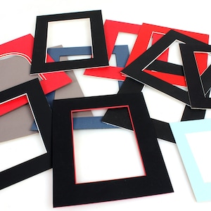 Può includere: Assortimento di passepartout neri, rossi e blu con aperture di diverse dimensioni. I passepartout sono realizzati in cartone spesso e hanno una finitura liscia.