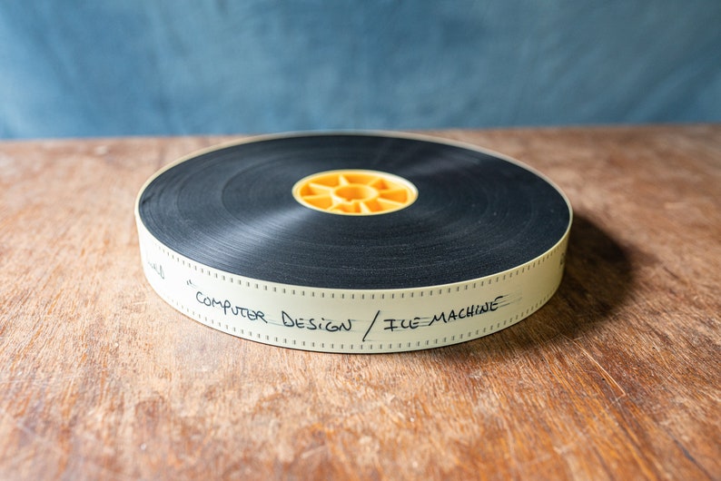 K&ouml;nnte beinhalten: Eine Schwarzwei&szlig;-Filmrolle mit einem wei&szlig;en Etikett, auf dem "COMPUTER DESIGN / TIME MACHINE" steht.