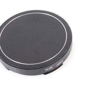 May include: Black camera lens cap with a silver rim and the text "MIR JAPAN" printed on the side.