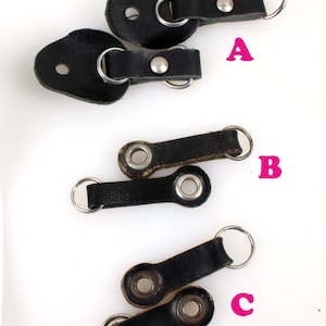 以下が含まれることがあります： 金属製のリングが付いた黒い革製のストラップループが3つあります。ループにはA、B、Cのラベルが付けられています。