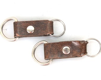 May include: Two brown leather keychains with silver metal rings and a silver button.