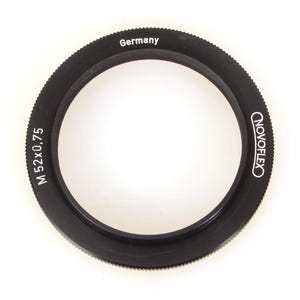 May include: Black Novoflex M52x0.75 lens adapter ring with the word "Germany" printed on the top. The adapter ring is circular with a ridged outer edge and the brand name "Novoflex" printed on the side.