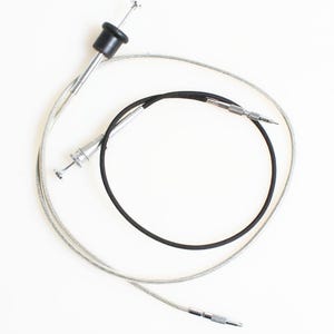 May include: A vintage camera cable release. It features a black rubber button, a silver metal cable, and a silver metal tip. The cable is coiled. This accessory is used to remotely trigger a camera's shutter.