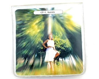 May include: A white card with a blurred image of a woman standing in a forest with a bright light shining through the trees. The text "CF-1, Aurora" is printed on the card.