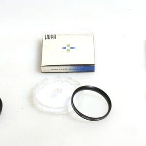 Könnte beinhalten: Drei Schachteln mit Nova-Kamer filtern, jede mit einem andersfarbigen Etikett. Die Schachteln sind geöffnet und zeigen die Filter im Inneren. Die Filter sind rund und schwarz, mit einer durchsichtigen Plastikabdeckung.