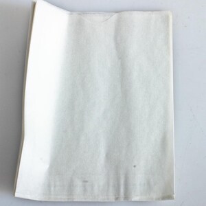 May include: A stack of folded, off-white tissue paper sheets. The paper has a slightly textured surface and is folded neatly, with a small, curved cut-out at the top. The paper is clean and appears unused.
