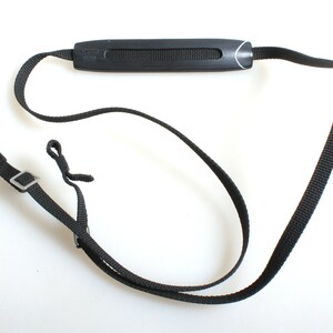 May include: Black camera strap with a padded black strap holder that says "Canon" in white lettering.