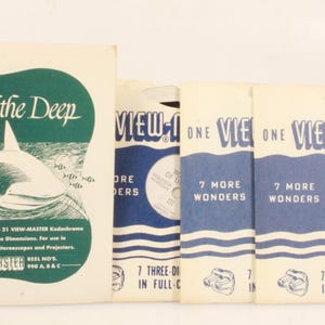 May include: Vintage View-Master reels and a booklet titled "Wonders of the Deep." The booklet features a shark illustration. The reels are labeled "7 More Wonders" and "View-Master Reel of the World." The items are in shades of green, white, and blue.