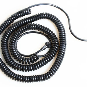 May include: A black coiled cable with a right-angle connector on one end and a round connector on the other end.