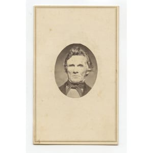 May include: A sepia-toned portrait of a man in a formal suit and bow tie, set within an oval frame. The photograph is mounted on a rectangular card with a decorative border, typical of vintage photography.