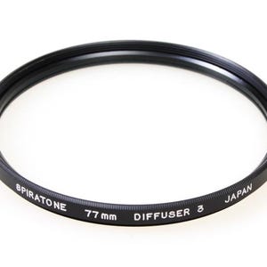 May include: A black Spiratone 77mm Diffuser 3 camera lens filter. The filter is a circular ring with the text "SPIRATONE", "77 mm", "DIFFUSER 3", and "JAPAN" printed in white. The filter is designed to fit a 77mm lens.
