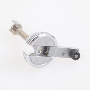 May include: A silver-toned, mechanical device with a cylindrical handle and a rotating dial. The device has a series of curved, fan-like blades and a central, elongated rod. A black knob is on the side. The device is on a white background.