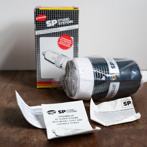 Puede incluir: Una unidad de flash blanca y negra con una caja negra etiquetada como "SP Studio Systems" y "SPSMOL VP AC Super Strobe with Model Light and Variable Power".