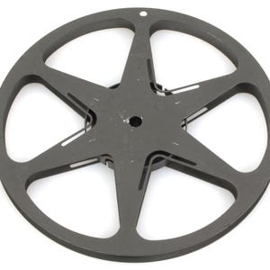 May include: A dark gray, star-shaped wheel with six points and a circular outer rim. The wheel has a central hole and several smaller openings. The object is made of metal and sits against a white background.