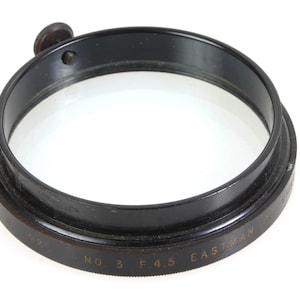 Könnte beinhalten: Schwarzer Metall-Objektivfilter mit einem klaren Glaszentrum. Der Filter trägt die Aufschrift "Eastman Kodak No. 3 F 4.5" am Rand.