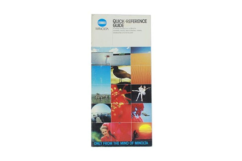 May include: A blue and white brochure with the text "Quick-Reference Guide" and "Minolta" on the front. The brochure features a collage of images, including a bird, a zebra, a sunset, and a ballerina.