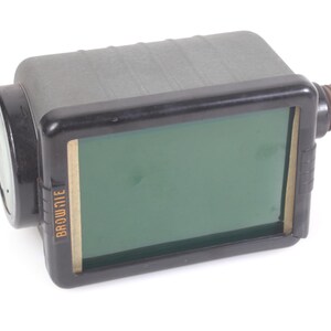 May include: A vintage camera with a rectangular body and a lens on the left. The camera has a black frame with a green screen and the word "BROWNI" printed on the side. It has a brown threaded piece on the right.