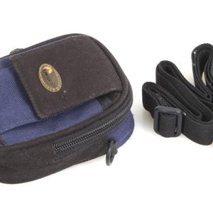 May include: A black and blue camera bag with a zipper closure and an adjustable strap. The bag has a small pocket on the front with the word "Domke" printed on it.