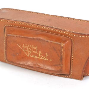 May include: A brown leather camera case with a gold "Stereo Realist" logo.