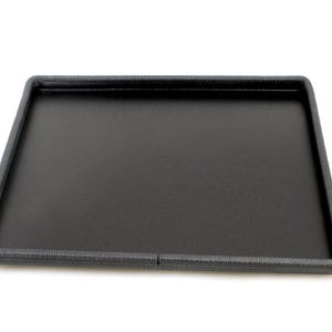 May include: A rectangular black tray with a textured border. The tray has a flat surface and a raised edge. The border is a darker shade of gray. The tray is on a white background.